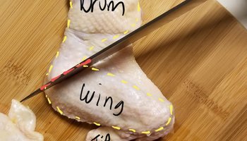 Raw chicken wing labeled drum, wing and tip, with a knife