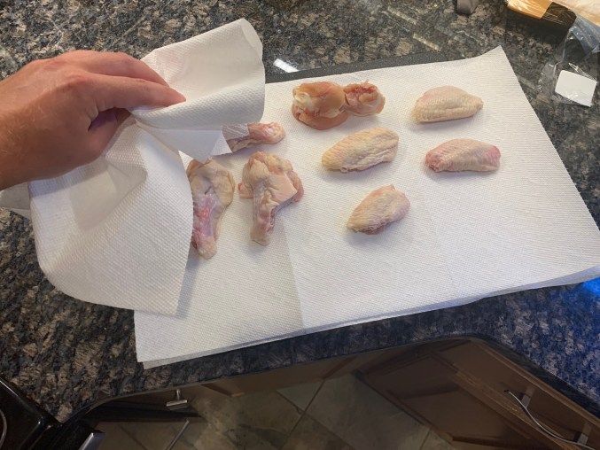 Patting raw chicken wings dry with paper towels on the counter