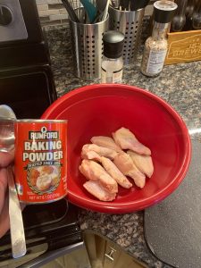 Raw chicken wings in a red bowl next to a can of baking powder