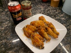 Sauced air fryer chicken wings on a white plate beside habanero pepper jam