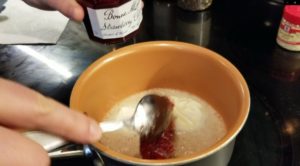 Spooning strawberry preserves into melted butter in a saucepan