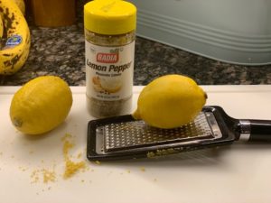 Two fresh lemons, a zester and lemon zest beside lemon pepper seasoning